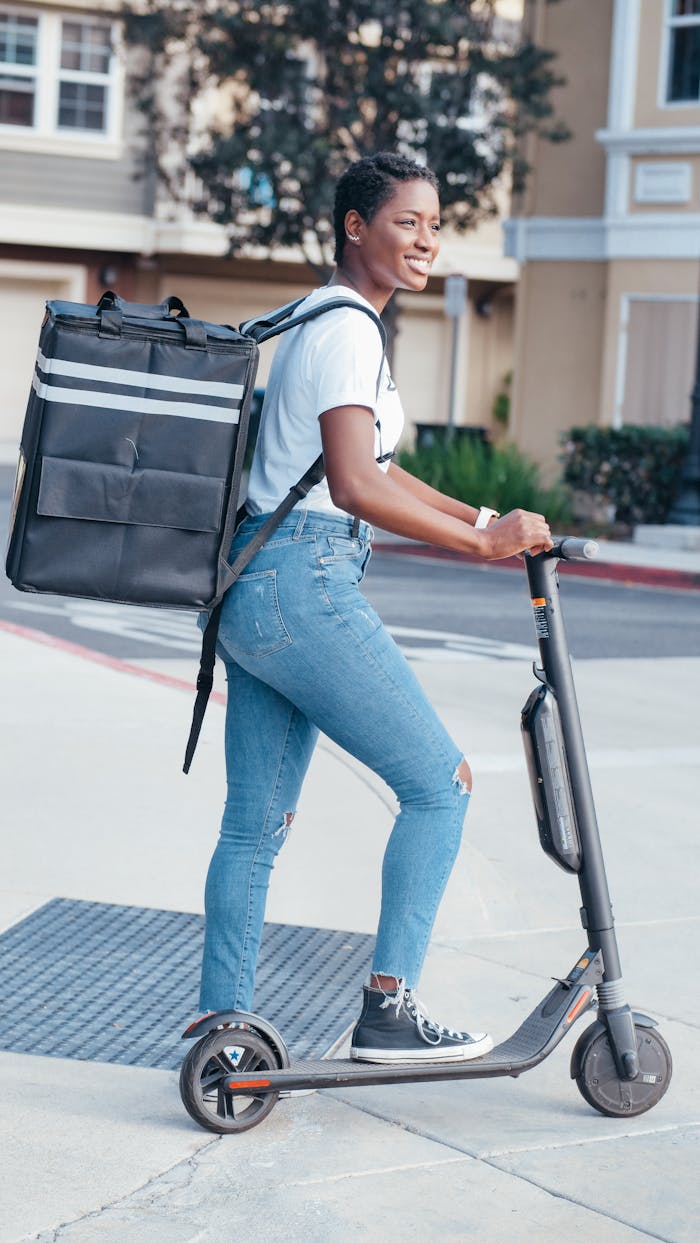 services-01 Smiling courier riding an electric scooter while delivering packages in a residential area.